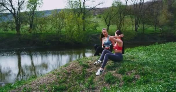 Mellett egy csodálatos folyó helyén két sportos hölgyek egy break idő eltarthat egy kis friss levegőt, miután a kemény edzés, hogy beszélgetni, és ivott egy kis vizet. 4k lassú mozgások. — Stock videók