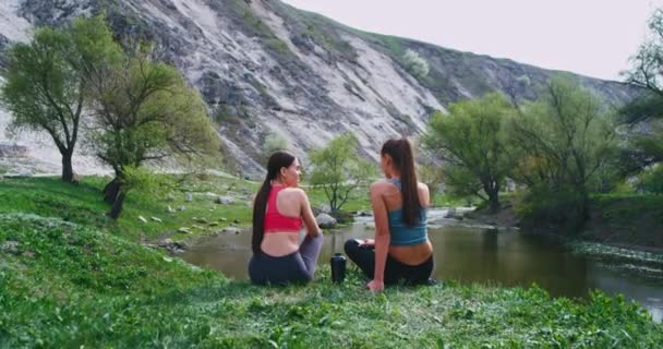 Две здоровые дамы после пробежки делают перерыв, пьют немного воды и расслабляются, чтобы подышать свежим воздухом и насладиться изумительным видом на пейзаж — стоковое видео