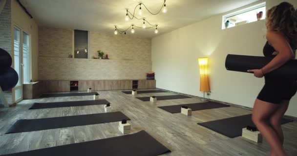 In een moderne wellness Yoga Studio vrouw wandelen met een sportmat door de studio die ze komt om een meditatie tijd voor zichzelf — Stockvideo