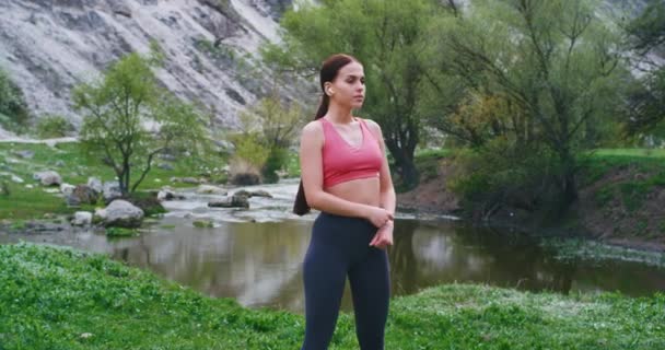 Привлекательная молодая женщина растягивая тело в то время как взять немного свежего воздуха на природе с красивым видом, йога время упражнения леди с подходящим телом в солнечный день — стоковое видео