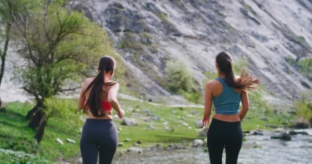 Happy fit dames die in het midden van de natuur rennen tijdens het luisteren naar muziek met draadloze airpods ze stopten voor een beetje op het dak van de rivier genieten van het landschap rond na een harde training — Stockvideo