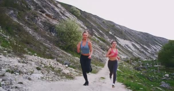 道路の石で山の真ん中を懸命に走っている2人のブルネットの女性は、彼らは素晴らしい晴れた日に一緒にワークアウトを楽しんで幸せです — ストック動画