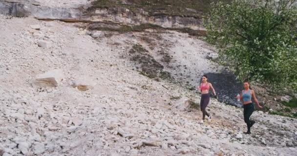 Två damer med en vältränad kropp efter en hård Workout dag genom bergsvägen törstig dricksvatten från en plastflaskor, de känner stor — Stockvideo