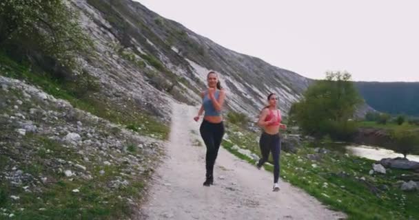 Mujeres muy hermosas en una ropa deportiva en medio del increíble paisaje de montaña corriendo juntas felices disfrutando del entrenamiento en la naturaleza con una hermosa vista — Vídeo de stock