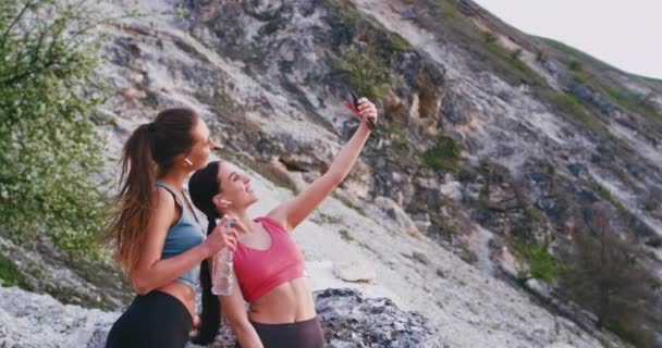 Selfie time for two charismatic ladies after the running workout smiling large take photos while holding the bottle of water — Stock Video