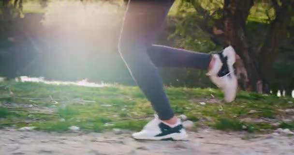 Detalhes de perto de uma senhora correndo na natureza através do campo de grama ao pôr do sol em segundo plano, estilo de vida de saúde para uma geração jovem. movimentos lentos — Vídeo de Stock