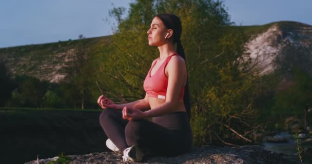 Mujer bonita haciendo su tiempo de meditación de yoga en la azotea del río en medio de la montaña, se concentró escuchando música de los airpods inalámbricos y tener un tiempo relajado — Vídeos de Stock