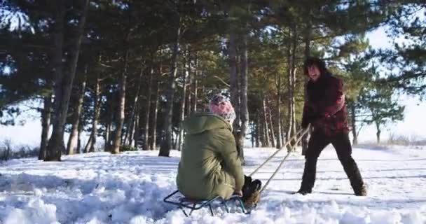 Lustige Momente mitten im Winter für ein Paar Mann und Frau beim Schlittenfahren und Spielen mit dem Schneeball — Stockvideo