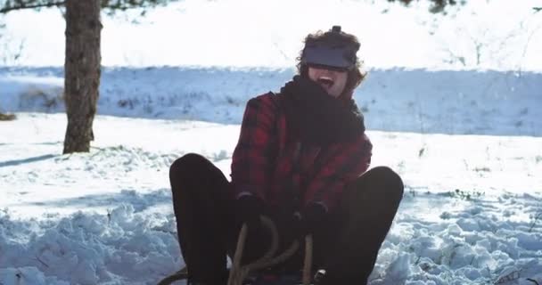 快乐魅力卷发的家伙在雪橇使用虚拟现实眼镜玩虚拟游戏，同时享受时间以外的冬季时间有乐趣 — 图库视频影像