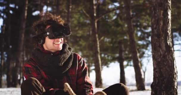 Sonriente retrato de tipo carismático usando unas gafas de realidad virtual jugando un juego mientras está sentado en el trineo en medio del día de invierno, disfrutando del juego en la naturaleza — Vídeos de Stock