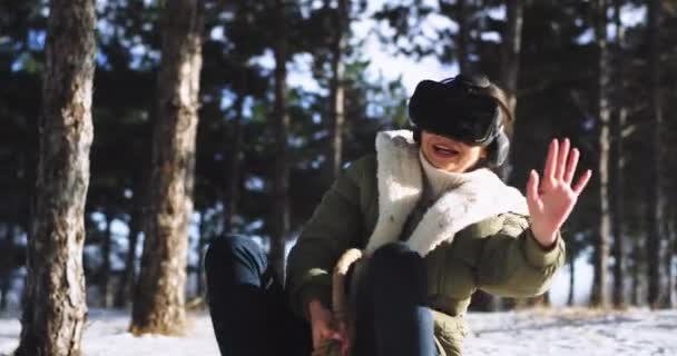 Mujer guapa explorando un nuevo juego virtual usando unas gafas de realidad virtual mientras está sentada en su trineo en medio del bosque nevado disfrutando del tiempo — Vídeo de stock