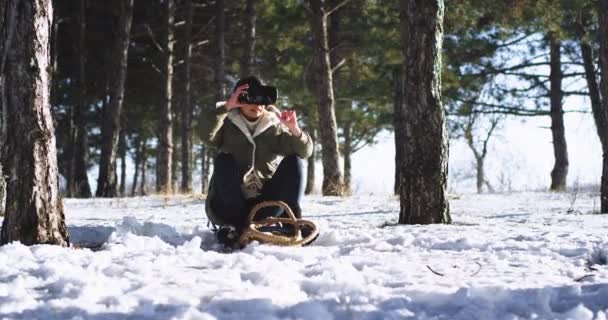 Азиатка, наслаждающаяся зимой на санях, с помощью очков виртуальной реальности выбирает игру и начинает играть, сидя на санях, наслаждаясь временем наедине с собой. — стоковое видео