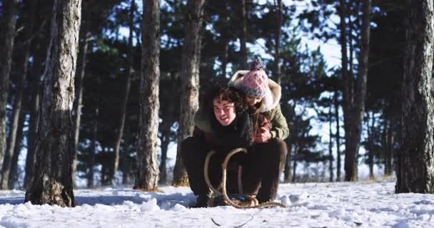 Snygg unga par multietniska har en rolig tid tillsammans i mitten av en snöig skog på släden de får rida för en släde rida äventyr — Stockvideo