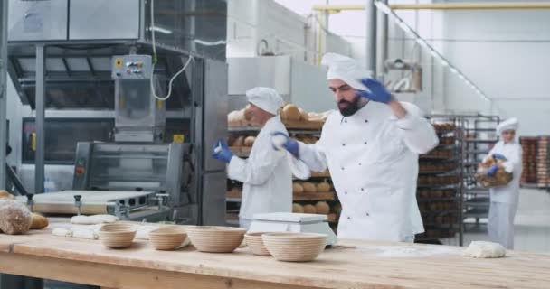 Танцы очень привлекательный пекарь человек с бородой, образуя куски теста для выпечки хлеба рядом с ним другие старые пекарь готовит хлебопекарные формы фоновые рабочие перемещения хлеба — стоковое видео