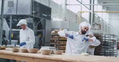 Fırın fabrikasında hevesli fırıncı adam sakallı dans ve hareketli komik ekmek pişirmek için hamur parçaları oluştururken diğer fırıncı şef hazır olsun makine arka plan işçileri ekmek koymak