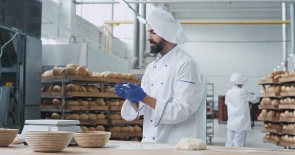 Due generazioni in un panificio industria vecchi e giovani panettieri godendo il lavoro insieme giovane con cuffie wireless ballare divertente mentre si prepara la pasta vecchio panettiere guardando lui e sorridente — Video Stock