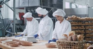 Güzel fırın fabrikası şık fırıncılar iki erkek ve bir kadın birlikte kamera ya da büyük gülümseyen ekmek pişirme için hamur parçaları oluşturan çalışma