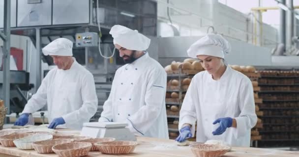 Donna attraente panettiere ei suoi colleghi panettieri che lavorano velocemente in un'industria di panetteria formando pezzi di processo di impasto di fare il pane in una cucina commerciale panetteria — Video Stock