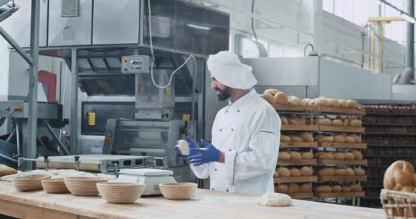 Padeiro com uma barba dançando engraçado em uma cozinha da indústria da padaria enquanto prepara a massa para assar pão, fábrica de alimentos — Vídeo de Stock