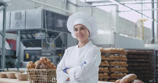 Portret uśmiechniętej dużej pięknej kobiety piekarz w stylowym mundurze patrzy prosto do aparatu przekroczyła ręce w fabryce piekarni — Wideo stockowe