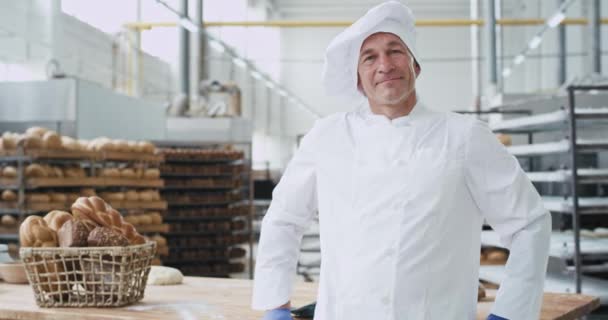 Dobrý vypadající zralý pekař ve velkém pekárenských branži, který se hodně usmívá a ukazuje velké jako před kamerou na pozadí. — Stock video