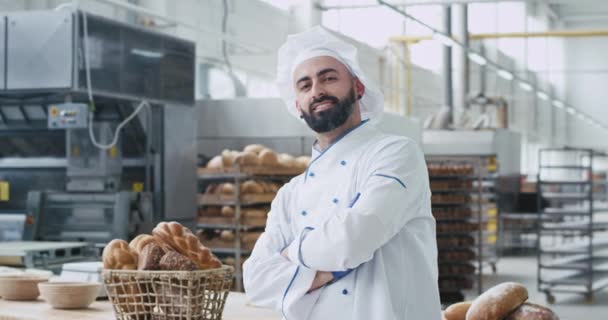 Bakery industry baker chef man with a beard looking straight to the camera smiling large while standing beside his work tablet , then taking details of a bakery basket with organic bread — Stock Video