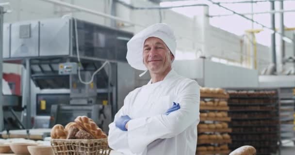 Vieil homme boulanger portrait regardant directement à la caméra dans une grande industrie de la boulangerie il profiter du temps sur son lieu de travail — Video