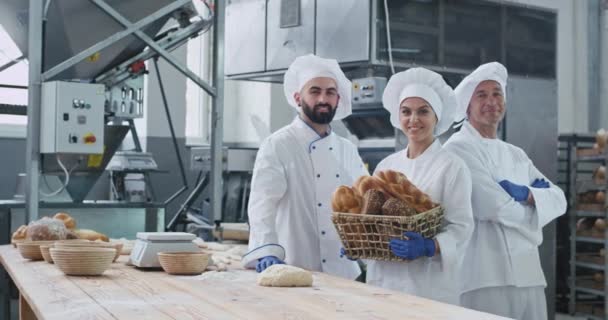 工业面包店两男一女面包师肖像直视镜头和微笑的大女人拿着篮子有机面包 — 图库视频影像