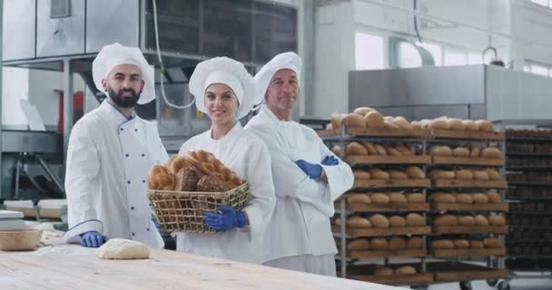 Boulangers femmes et hommes dans une grande boulangerie souriant grand à la caméra tout en tenant un panier de pain bio — Video