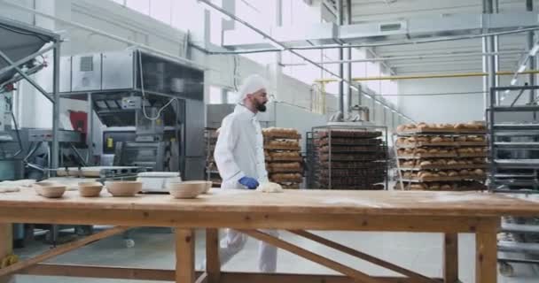 Charismatischer Bäcker mit Bart, der lustig an seinem Arbeitstisch tanzt, während er in einer großen Bäckereifabrik den Teig für das Brotbacken vorbereitet — Stockvideo