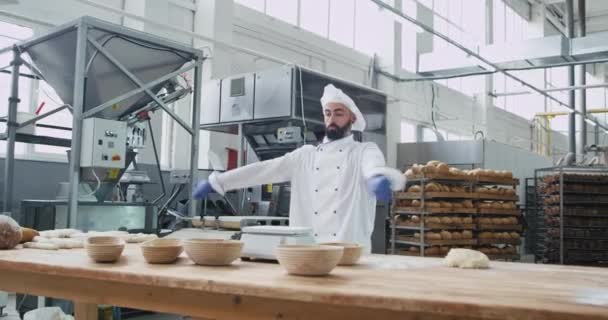 Homem atraente padeiro com um queixo em um uniforme elegante dançando engraçado em seu trabalho de mesa em uma indústria de panificação ele aproveitando o tempo enquanto prepara a massa para ser cozido — Vídeo de Stock