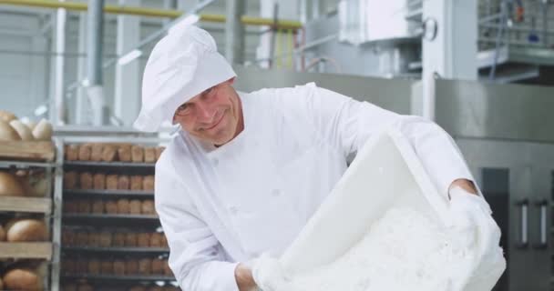 Bello sorridente vecchio panettiere preparare l'impasto aggiunge farina in un contenitore industriale primo piano guarda dritto alla fotocamera Ana s hanno un bel volti felici. 4k — Video Stock