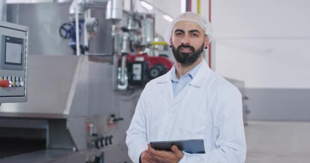 Man engineer with a tablet and his assistance on the background closeup portrait looking straight to the camera smiling , woman holding a map and make a check in of the machine. 4k — Stock Video