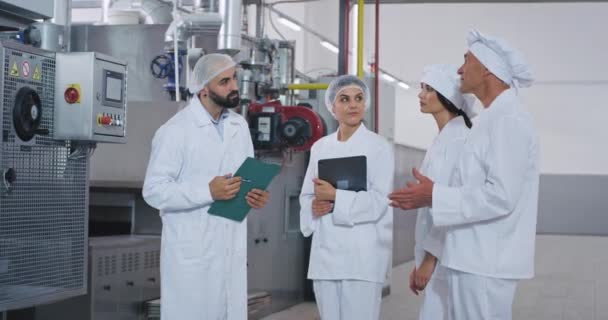Baker chef gammal man och ung ingenjör kille med skägg har ett samtal med deras hjälp i mitten av bageriindustrin fabriken — Stockvideo