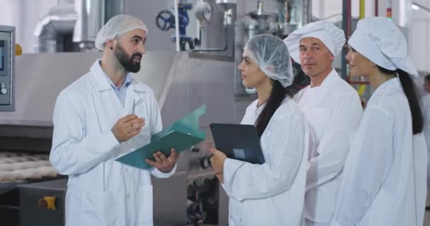 Grupo de trabajadores de la industria de panadería ingeniero explicando el plan de seguridad para la máquina industrial viejo panadero y sus asistencias listado muy concentrado — Vídeos de Stock