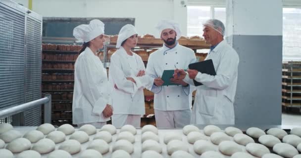 In einer Bäckereifabrik zwei Bäcker Koch eine Assistentin auflistet konzentriert ihren Ingenieur alten Mann mit einer Karte erklärt etwas über die Industriemaschine — Stockvideo