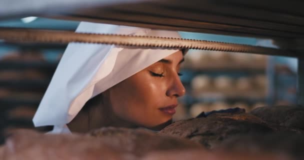 Gros plan look parfait de la jeune femme boulangère dans une boulangerie, elle sentait excité le pain frais cuit au four et prendre un peu de l'étagère industrielle — Video