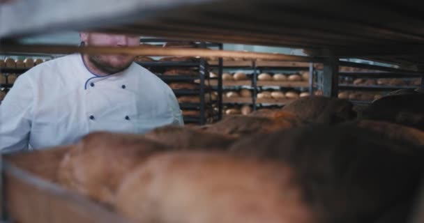 Харизматичный большой человек пекарь в форме крупным планом в пекарне кухне он с удовольствием пахнет свежим хлебом с промышленной полки — стоковое видео