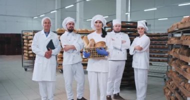 Gıda endüstrisi güzel bayan fırıncı ve meslektaşları ana ekip kamera ve büyük bir fırın sektöründe gülümseme düz bakıyor