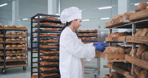 Charismatische reife Bäckerin in schöner weißer Uniform überprüft das frische Brot und stellt es auf die Bestellung in die Regale — Stockvideo