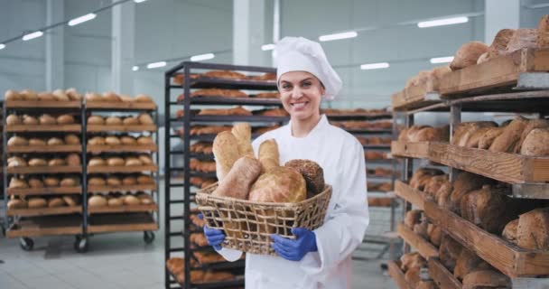 Mosolygó nagy karizmatikus érett Baker nő, aki egy Vintage kosár szerves kenyeret, és egyenesen a kamera háttérben nagy pékség ipar — Stock videók