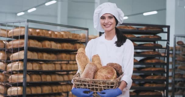 Fábrica de alimentos sonriendo gran hermosa dama en la sección de hornear que sostiene un pan recién horneado y mirando directamente a la cámara . — Vídeos de Stock