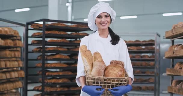 Padaria indústria senhora carismática com uma grande cesta de pão orgânico no meio da máquina industrial olhando diretamente para a câmera e fazer um sorriso feliz rostos — Vídeo de Stock