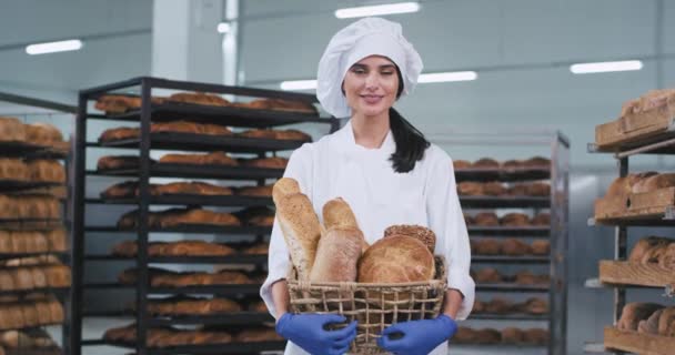 Μια χαριτωμένη χώρα νεαρή γυναίκα φούρναρης σε μια βιομηχανία αρτοποιίας κρατώντας ένα καλάθι με φρέσκο ψωμί και χαμογελαστή χαριτωμένη — Αρχείο Βίντεο