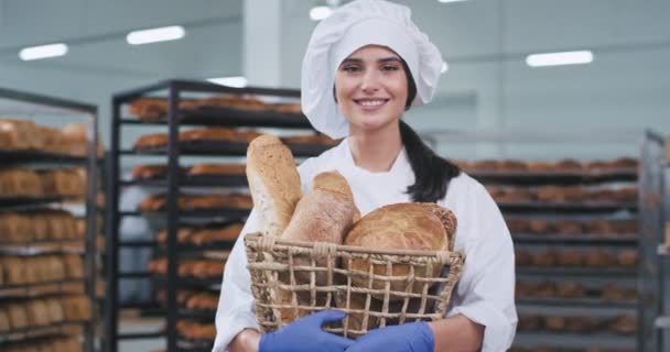 O sevimli bir gülümseme yapmak taze pişmiş ekmek ile bir sepet tutan kamera önünde bir fırın sektöründe bir ülke bayan fırıncı Portresi — Stok video