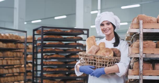 Beyaz üniformalı güzel bayan fırıncı taze ekmek ile bir sepet tutan ve kamera önünde sevimli gülümseyen — Stok video