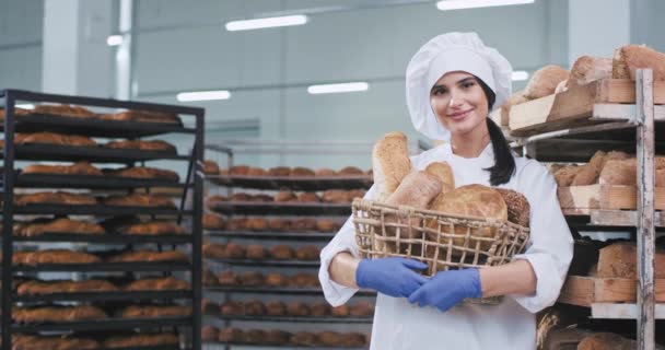 Хлібопекарська промисловість молода жінка пекарня з кошиком свіжого запеченого хліба дивиться прямо на камеру і досить посміхається — стокове відео