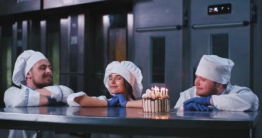Siyah saçlı çekici bir kadın, bir dilek yapar ve mumlar dışarı üfler ve sonra sakallı iki tombul erkek kucaklar sonra