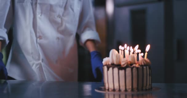 Eine junge schöne Dame mit blauen Handschuhen und Kochuniform bläst die Kerzen auf der Torte aus — Stockvideo