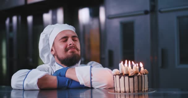 Очаровательный человек в шляпе шеф-повара задувает свечи на божественном торте на день рождения — стоковое видео